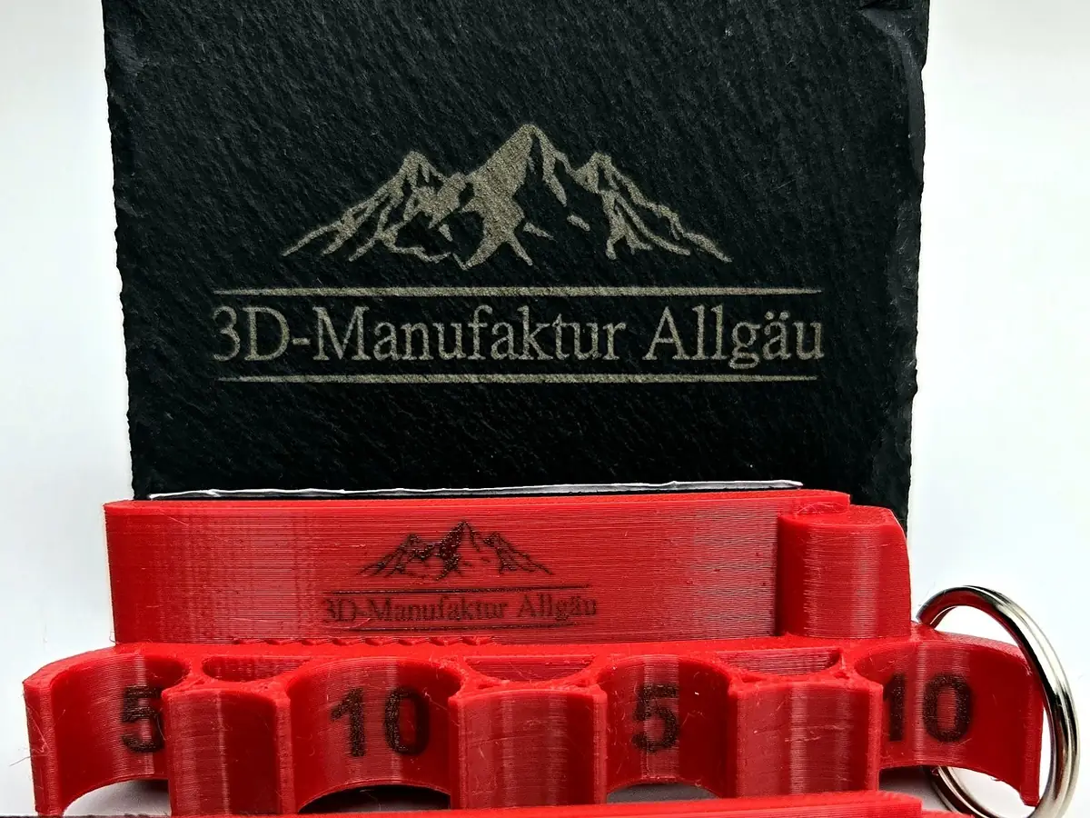 Roter Spritzenhalter 2.0 mit eingraviertem Logo vor einer gravierten Schieferplatte